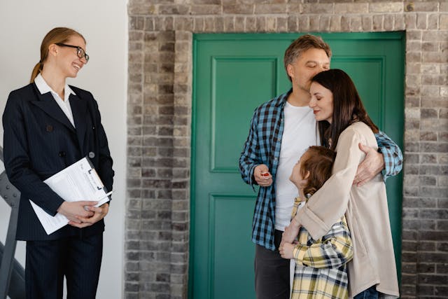 People standing in the entryway of a home while three of them hug and another person stands near, smiling, them holding a clipboard